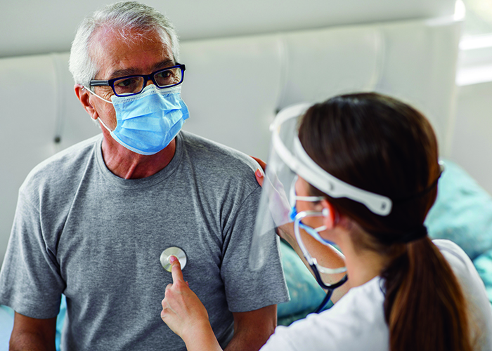 A masked male patient having his heart checked with a stethoscope by a masked female clinician.