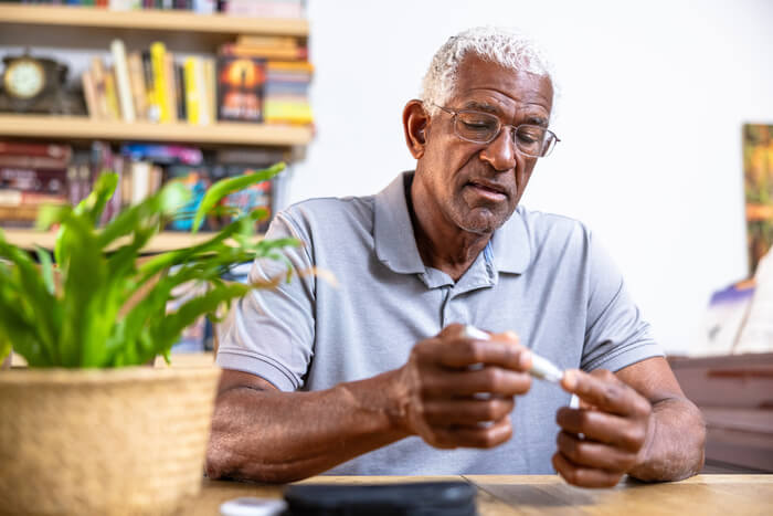 Older man sitting at a table testing his blood sugar.