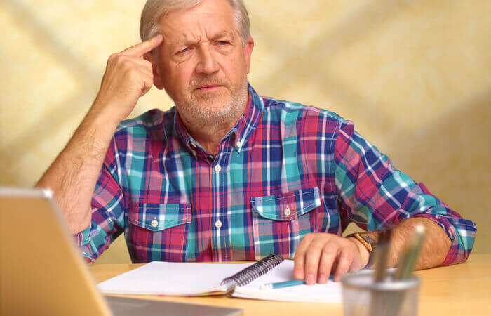 Older man in plain shirt holding hand to head in confusion.