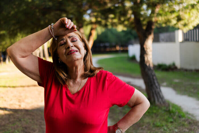 Overheated woman in red shirt trying to cool off outdoors.