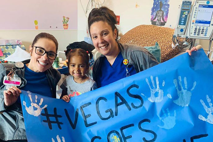 Pediatric patient holding #VegasGoesBlue window banner with nurses