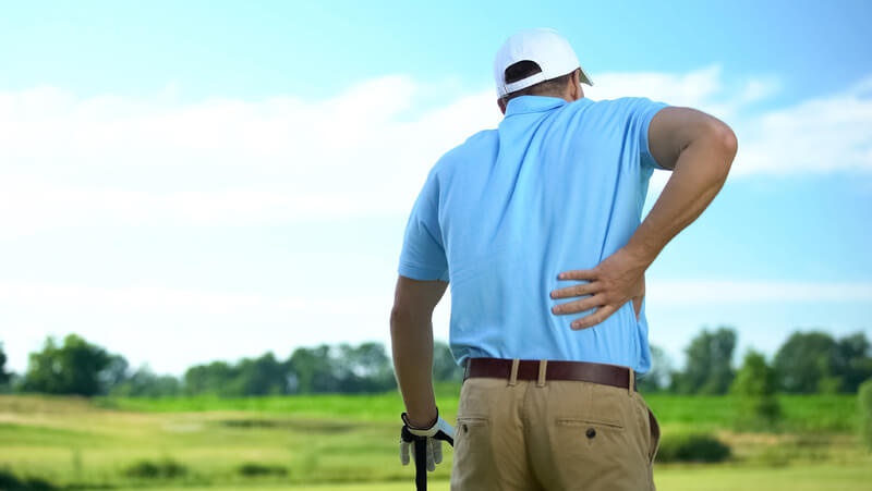 Man on golf course grips his back indicating pain.