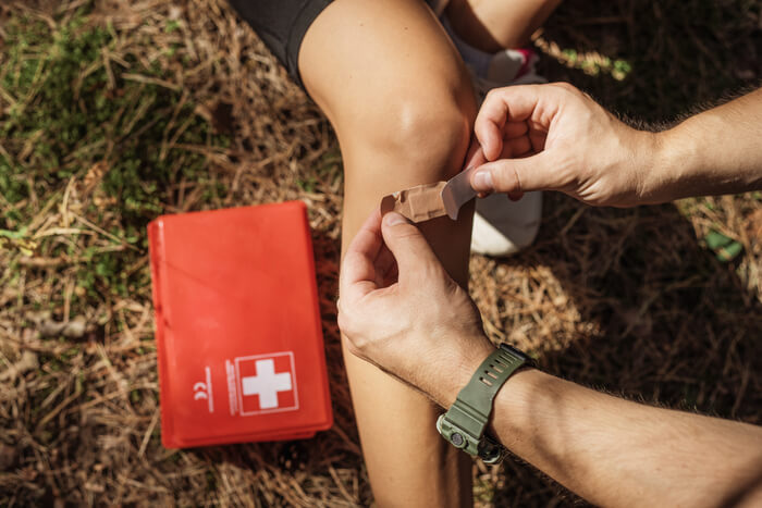 Red first aid kit beside a bandage being applied to a knee.