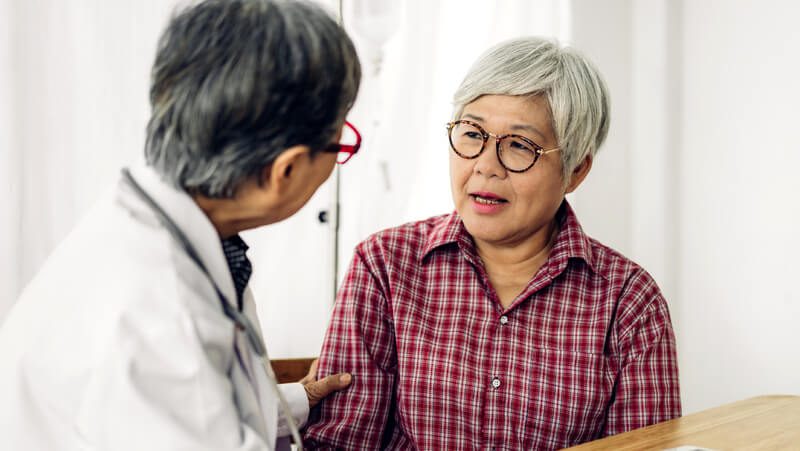 Concerned-looking woman consulting with clinician in white coat.