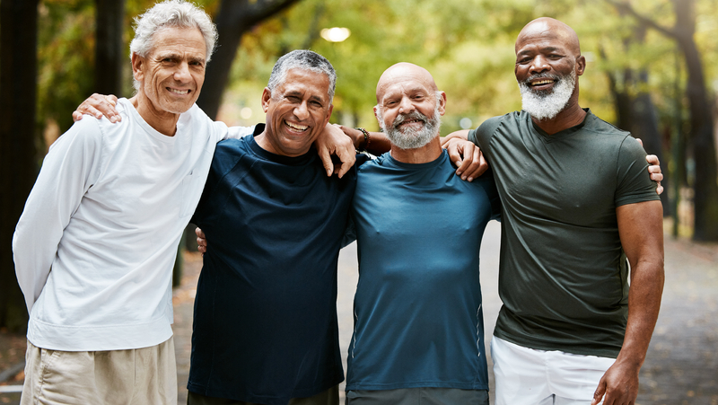 Four men smiling together on an outdoor walking trail.