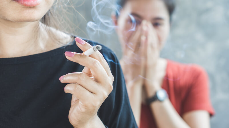Close-up of woman smoking a cigarette with smoke bothering a second woman.