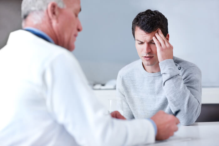 Man holding head in pain in doctor's office.