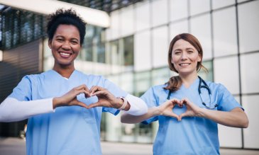 Two medical professionals show hearts with their hands while smiling 
