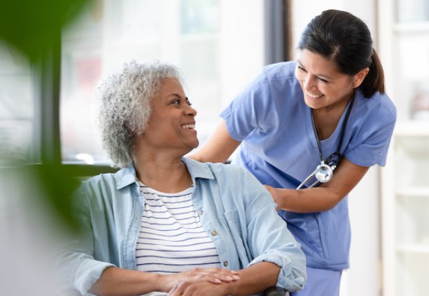 A female patient in a wheelchair smiling at a female nurse