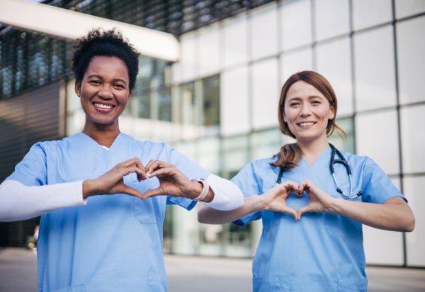 Two medical professionals show hearts with their hands while smiling 