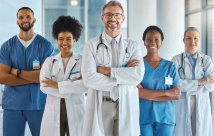 Stock photo of five medical professionals standing in a line with their arms crossed and smiling