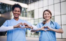 Two medical professionals show hearts with their hands while smiling