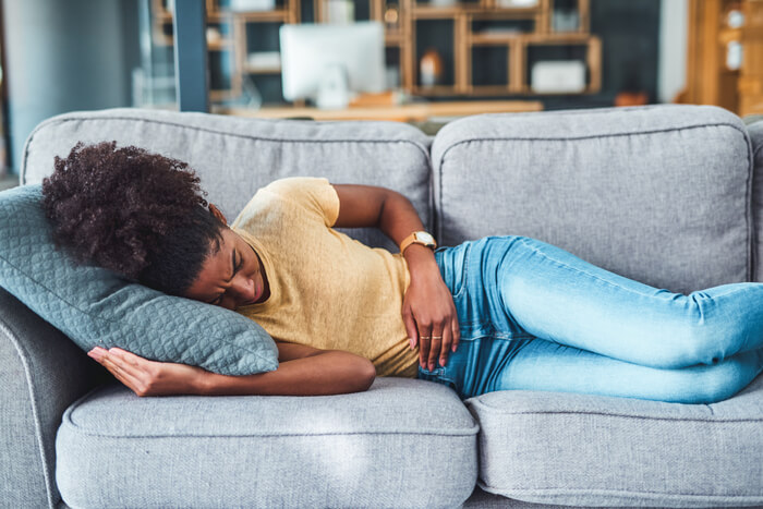 Woman lying on couch gripping stomach in pain.